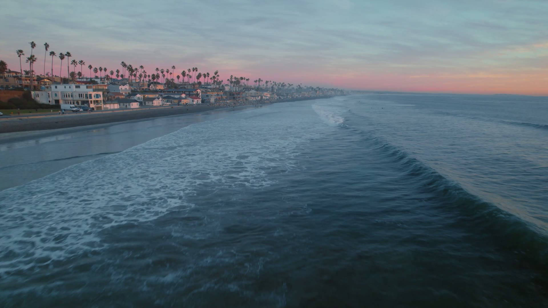 Aerial view of a Southern California coastal neighborhood at sunset, with palm-lined streets meeting the Pacific Ocean.